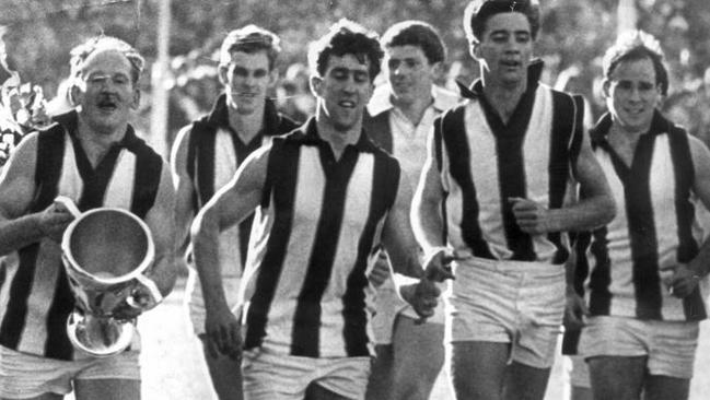 St Kilda skipper Darrel Baldock carries the 1966 premiership cup as his Saints teammates wear Collingwood jumpers, with the exception of Ian Synman (third from right).