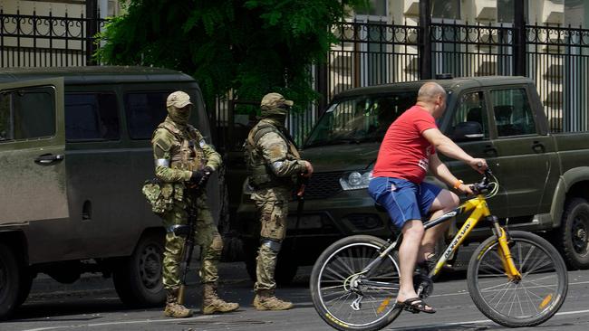 A man rides a bicycle past members of the Wagner mercenary group, pictured standing guard in the city of Rostov-on-Don on the weekend during their short-lived insurrection. Picture: AFP