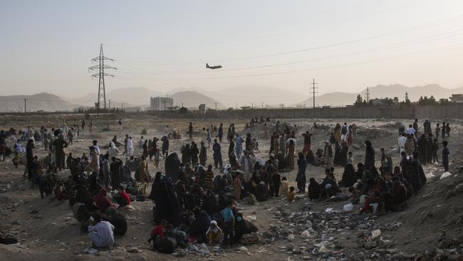 Hundreds of people camp in a dusty field outside Hamid Karzai International Airport, Kabul as a US military C-17 transport aircraft takes off in the background. Picture: Andrew Quilty