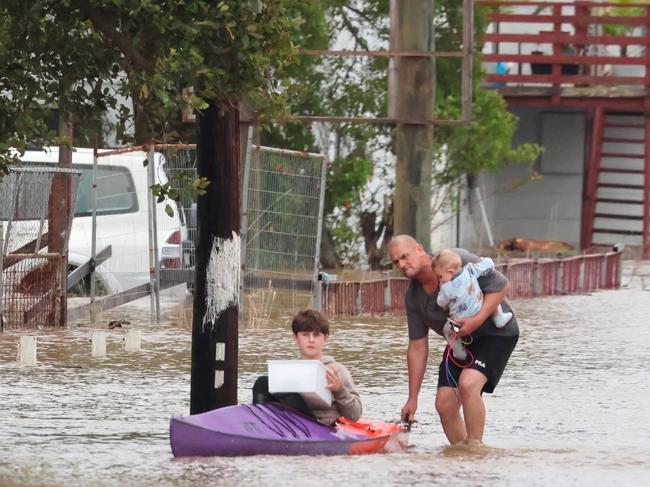 A dad pushes his son through floodwaters in Port Macquarie, holding his baby in the other hand. Picture: Facebook/Adam Dederer