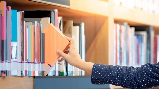 Generic image of a man picking books from a shelf at a library.