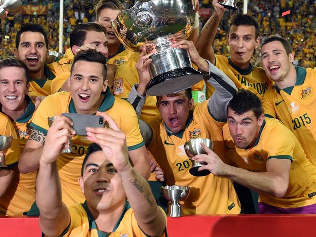 Australia's Massimo Luongo (C) takes a selfie as the team celebrates with the AFC Asian Cup football trophy after beating South Korea at Stadium Australia in Sydney on January 31, 2015. AFP PHOTO / Saeed KHAN -- IMAGE RESTRICTED TO EDITORIAL USE - STRICTLY NO COMMERCIAL USE