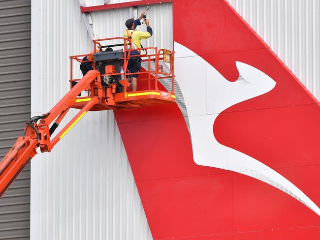 Workmen are seen working on the Qantas flying kangaroo logo on the side of the Qantas maintenance facility building at Brisbane Airport in Brisbane, Wednesday, March 25, 2020. Qantas has cut its domestic flying capacity by 60 per cent and stood down 20,000 staff. (AAP Image/Darren England) NO ARCHIVING