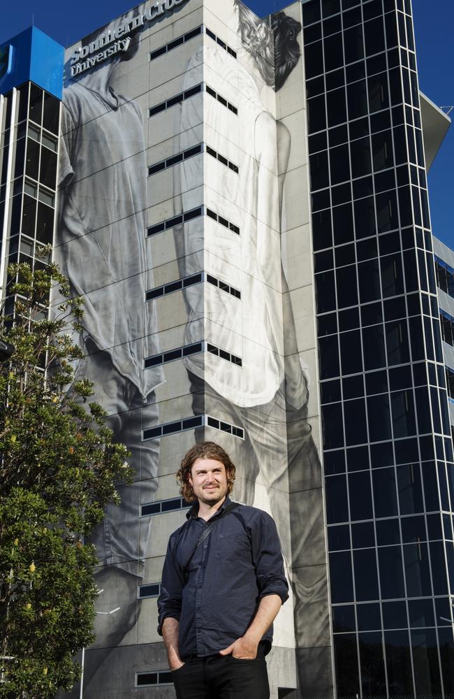 Internationally renowned mural artist Guido van Helten in front of his large scale artwork on a side of a building at Southern Cross University Gold Coast campus. Photo: Elise Derwin