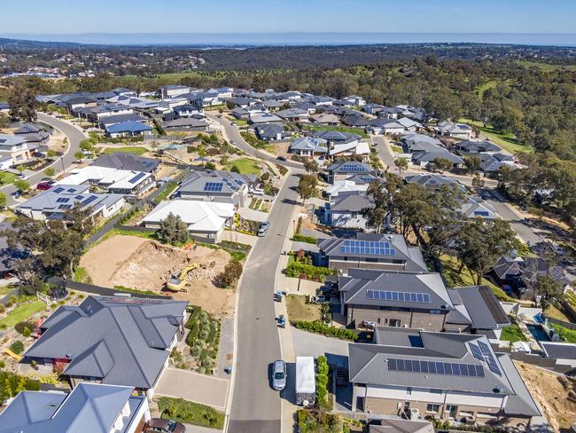 Aerial view of houses and streets in new wealthy suburb in Adelaide foothills with construction in foreground and coastline in background: large houses, landscaped gardens, rooftop solar systems,