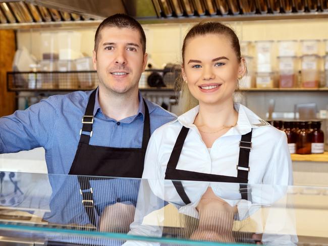 CAREERS FOR MAY 2: Portrait of small business owner smiling behind counter inside eatery, Successful young waiters working in apron holding food order for home delivery