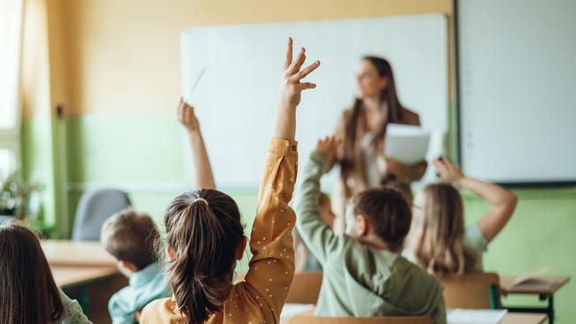 Students raising hands while teacher asking them questions in classroom