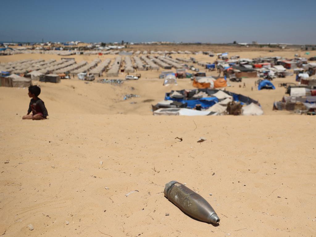 An unexploded shell lies on a sand dune as a young boy sits near a makeshift camp for displaced Palestinians in the area of Tel al-Sultan in Rafah.