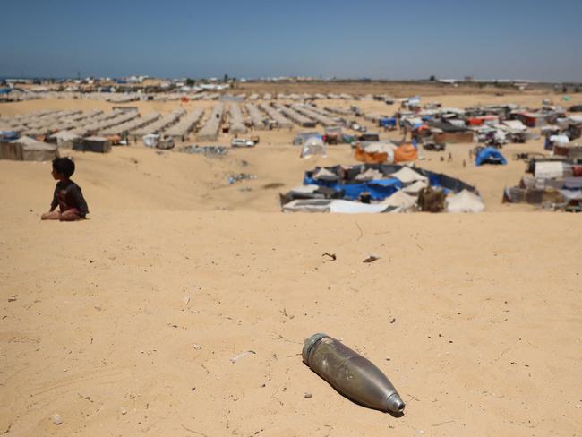 An unexploded shell lies on a sand dune as a young boy sits near a makeshift camp for displaced Palestinians in the area of Tel al-Sultan in Rafah.