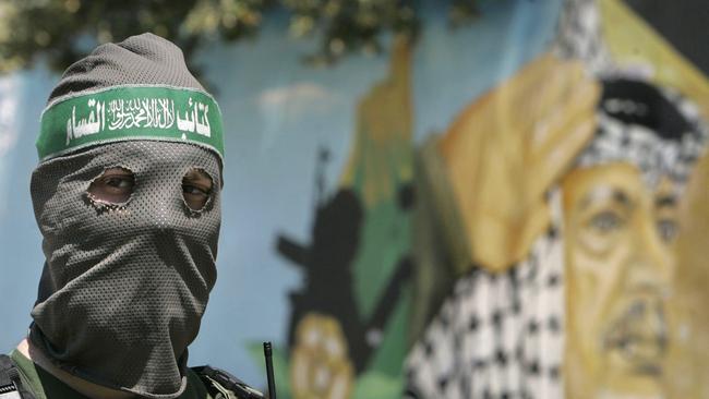 Hamas militant standing guard in front of mural of former Palestinian leader Yasser Arafat in Gaza City, 2007.