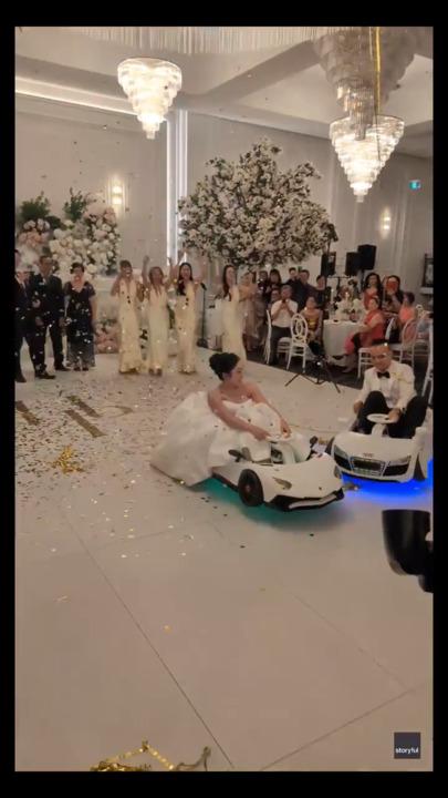 Bride and groom drift into wedding reception in electric toy cars