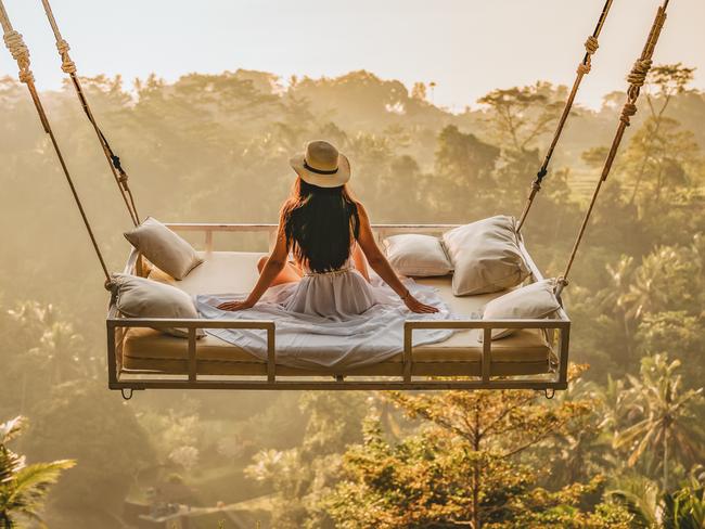 Photo of a young woman sitting on the swing.  Jungle Bed hanging over the tropical forest with Caucasian female resting while looking at the view, Bali, Indonesia. Rear view of a female sitting and enjoying the view.Escape 19 May 2024Doc HolidayPhoto - iStock