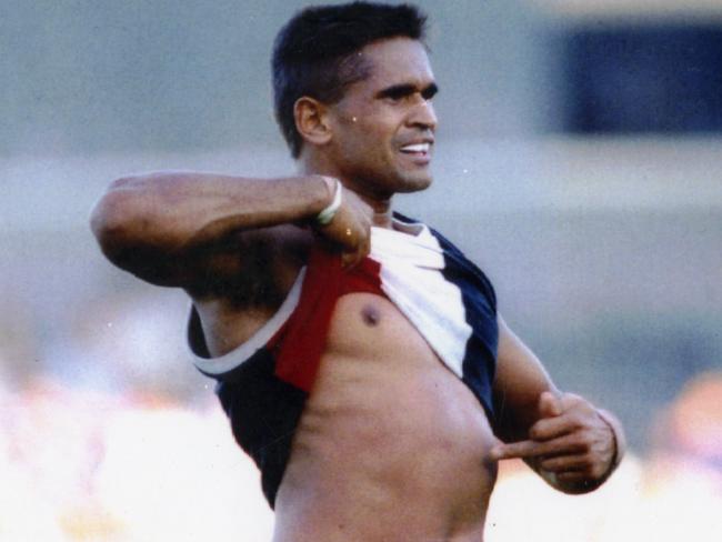 Nicky Winmar lifts his jumper and points to his skin.