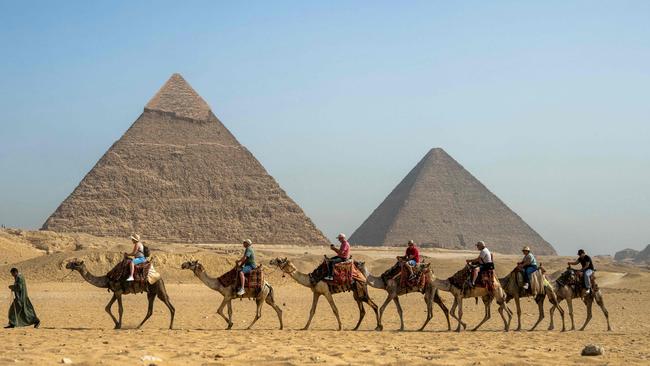 A guide pulls a lead camel as tourists ride in a row past the Great Pyramid of Khufu and the Pyramid of Khafre on the outskirts of Giza. Picture: AFP