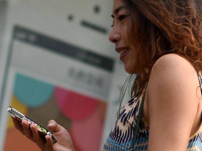 A woman looks at her mobile phone as she walks past an Apple iPhone 5 poster outside a store in Beijing on September 11, 2013. Apple's lower-cost iPhone 5C will retail for more than 700 USD in China, putting it out of reach of most consumers and raising questions over the firm's ability to build sales in the world's biggest mobile market. AFP PHOTO / WANG ZHAO