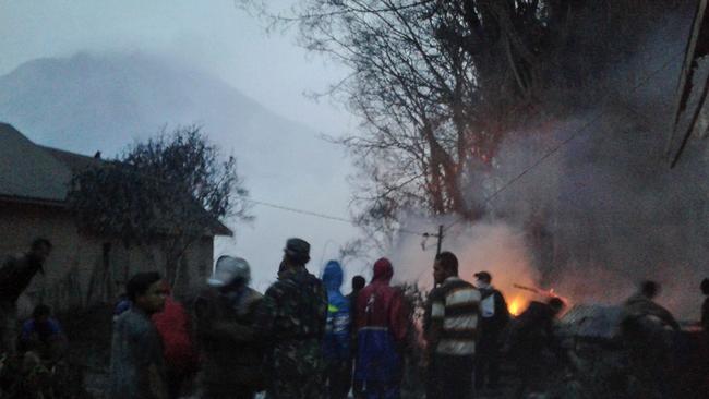 Villagers and rescuers stand near a burning tree after it was hit by pyroclastic flows from the eruption of Mount Sinabung, background, in Gamber, North Sumatra, Indonesia. Picture: AP