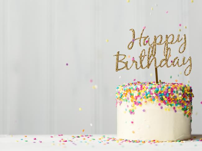 Colorful birthday cake with golden happy birthday banner and falling sprinkles