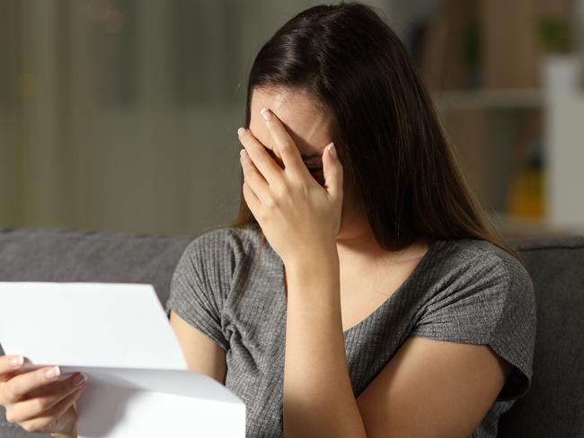 Sad woman reading a letter in the dark at home, renter, tenant, eviction, bill, stress, anxiety - for Herald Sun realestate