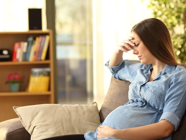 Worried pregnant woman sitting on a couch in the living room at home