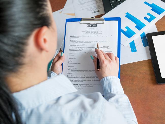 CAREERS: Young businesswoman or recruiter reviewing resume for opening position, sitting at the desk with laptop and documents in office