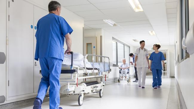 Male nurse pushing stretcher gurney bed in hospital corridor with doctors &amp; senior female patient