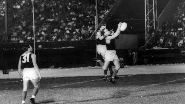 Melbourne captain Ron Barassi watches his teammates, Ray Dawson (in front) and Barry Bourke, contest a mark in an exhibition of Australian rules football under lights at Hickam airfield, Honolulu in 1963. Picture: Archives.