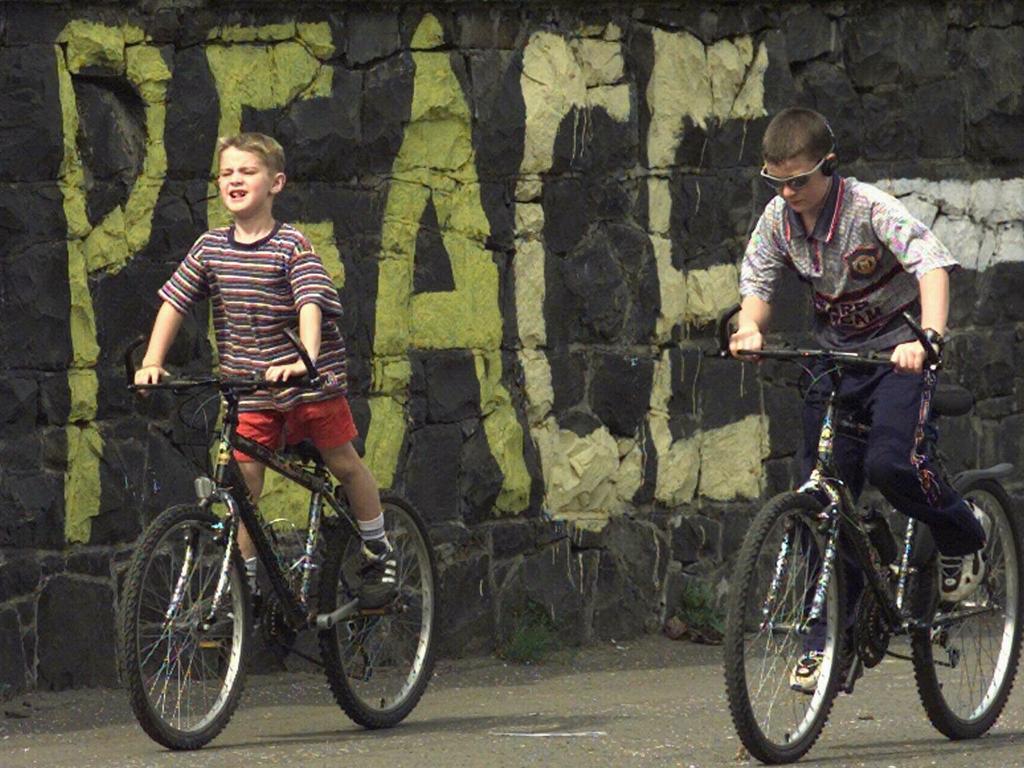 Two boys ride past a graffiti-covered wall in west Belfast after resumption of the IRA ceasefire on June 20, 1997.