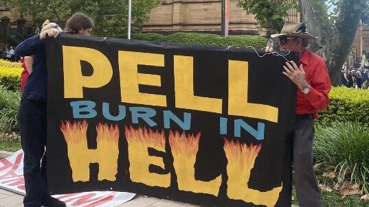 Protesters hold a sign which reads "Pell Burn in hell" near St Mary’s Cathedral on Thursday.