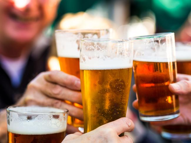 Close up color image depicting a group of people celebrating with a toast. The people cheers their glasses of beer (pints of beer) together in a gesture of celebration, togetherness and happiness. The people are defocused in the background, while focus is on the glasses of beer in the foreground. Room for copy space.