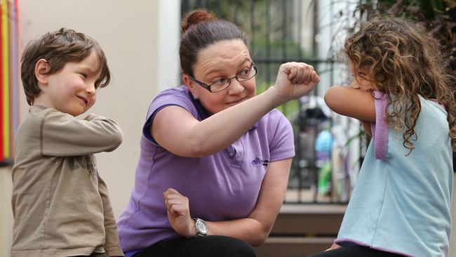 Childcare worker Hannah McKeller shows Jack and Winnie how to control a sneeze so germs don’t spread. Picture: Richard Dobson