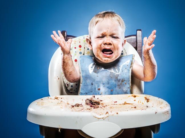 A one year old child sitting in a highchair and covered with his meal. A typical day in life of a baby.