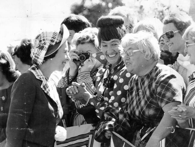 A woman takes a photo of the Queen as she stops to talk with one of the thousands of well-wishers who packed the streets of Elizabeth.