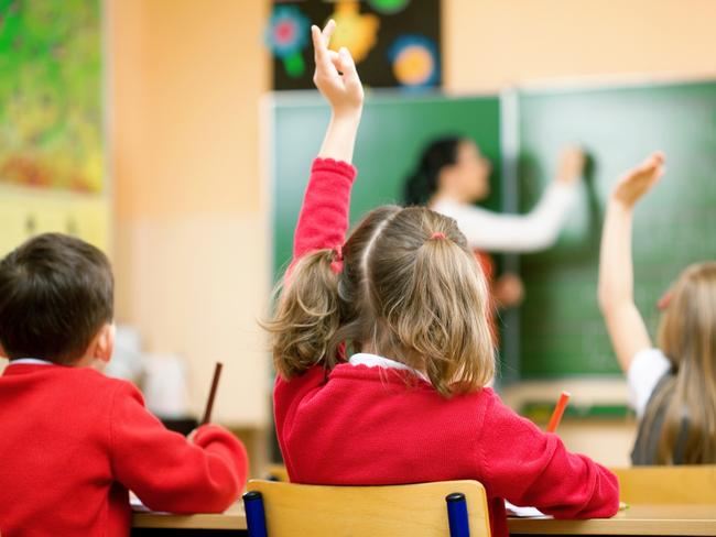 Elementary school kids raising their hands in class to answer a teacher's question.