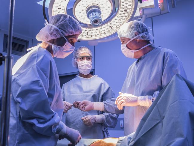 Doctors wearing surgical masks and gowns performing an operation on patient in hospital operating theater.
