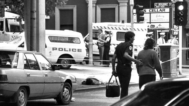 An ambulance officer escorts a woman to safety past the body of gunman Frank Vitkovic on the footpath.