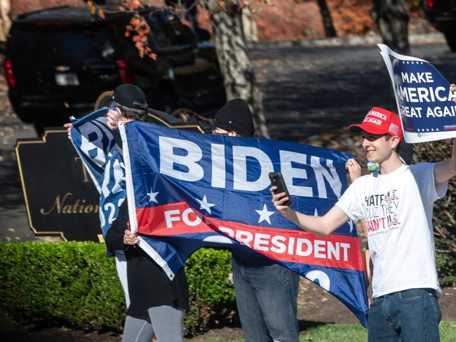 Biden and Trump supporters wave flags as Mr Trump’s motorcade enters his golf club in Virginia. Picture: AFP