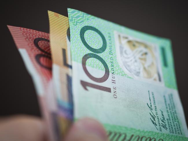 A hand holding a 20,50 and 100 Australian dollar notes on a black background