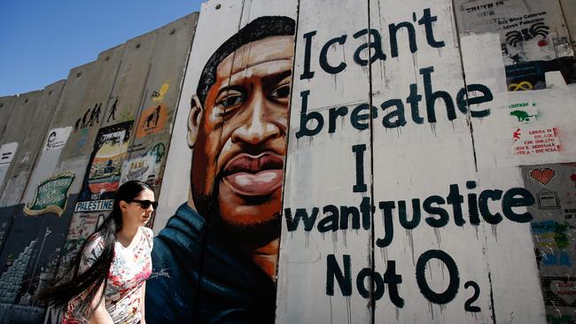 A woman walks past a mural showing the face of George Floyd.