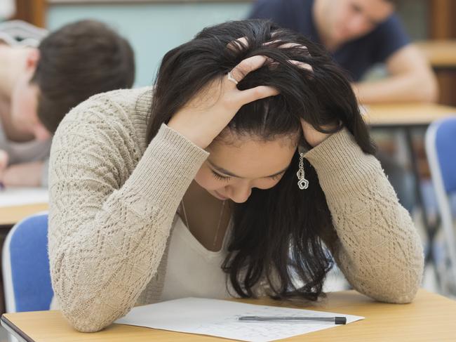 Stressed student sitting in a classroom at a table while doing an exam- STOCK PIC