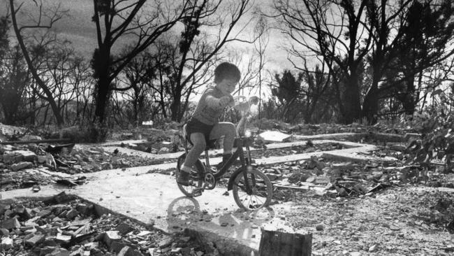 A young child riding his bicycle on the exposed foundations of a house that was destroyed by the Ash Wednesday bushfires.