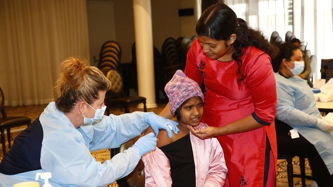 Sharon Bose braves the vaccine from nurse Melanie Broadbent while her mother Akhila Bose lends support. Picture: John Appleyard