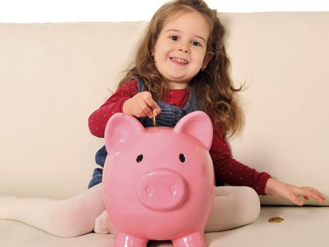 Happy little girl putting coin into huge piggy bank on sofa