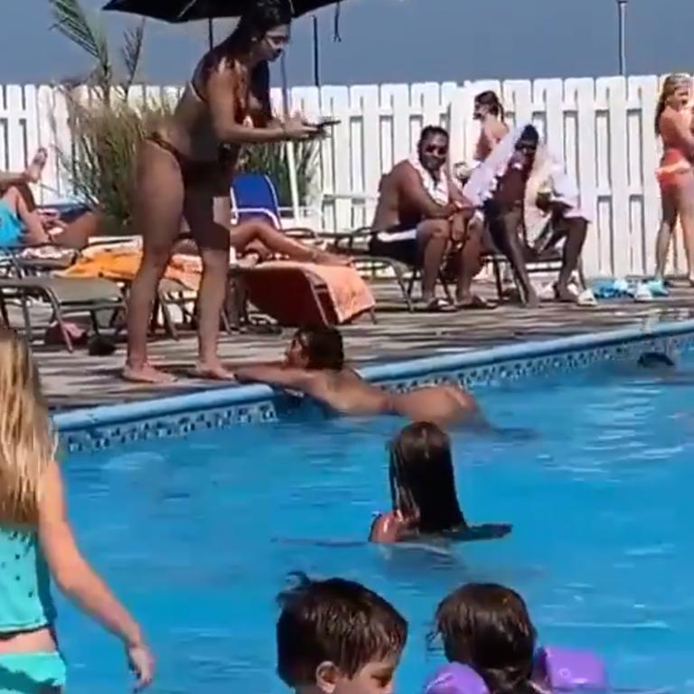 The woman raises herself out of the water while another woman takes a photo as children swim around her.