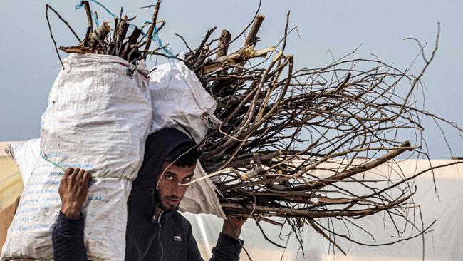 A man carries sacks loaded with salvaged firewood for campfires while walking past tents erected by Palestinians near the Egyptian border in Rafah. Picture: AFP