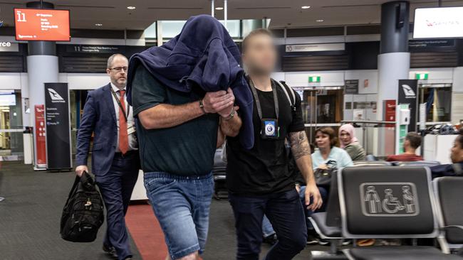 NSW detectives lead Caldow through the airport.