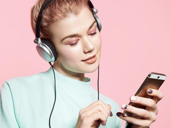 Beautiful young woman in headphones listening to music smiling with closed eyes standing on a pink background in a blue sweatshirt