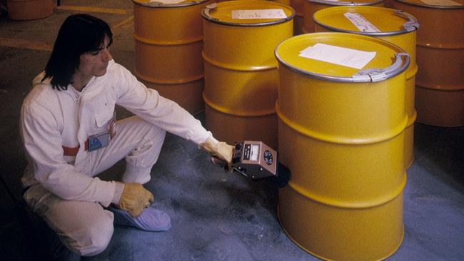 Nuclear decontamination worker using a Geiger counter to check radiation levels for barrels containing low-level radioactive waste. The waste was crushed and placed into barrels while decontaminating a radioactive nuclear site. The method of disposal depe