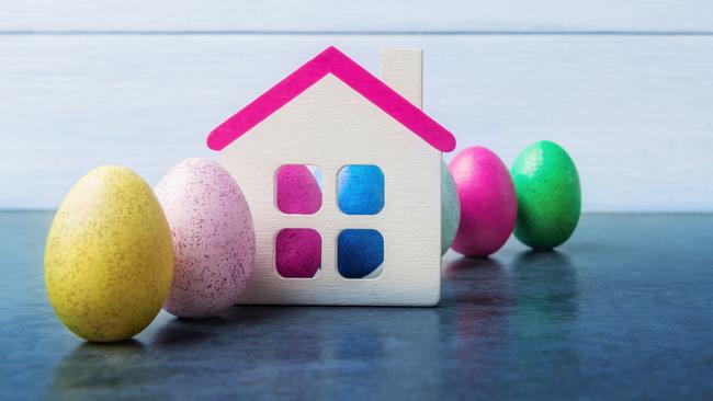 House model and multicolored Easter eggs over light blue wooden background. Generic egg housing