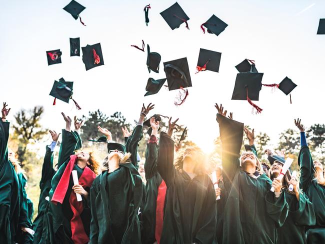 Generic stock photo showing a large group of happy college students celebrating their graduation day outdoors while throwing their caps up in the air.