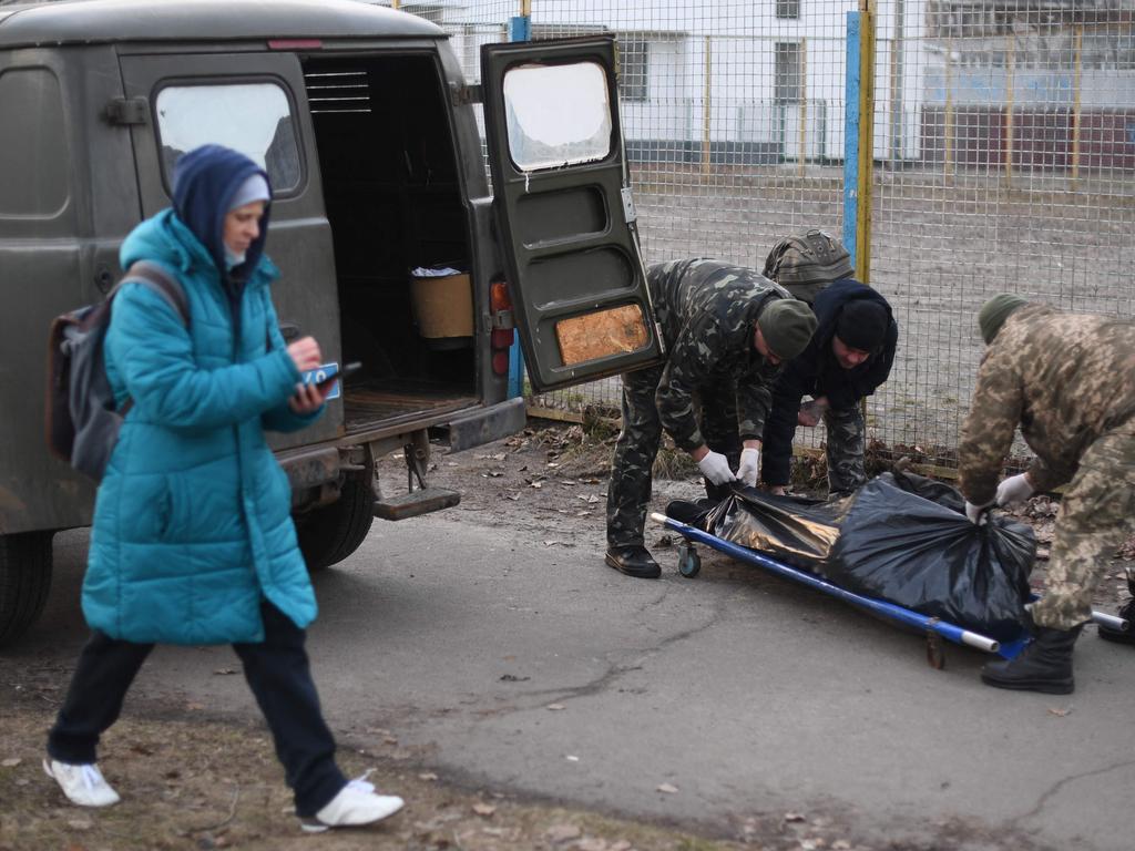 A woman walks as Ukrainian servicemen prepare to pick up the body of an Ukrainian man who was shot when a Russian armoured vehicle drove past him, on a sidewalk in the north of Kyiv. Picture: AFP